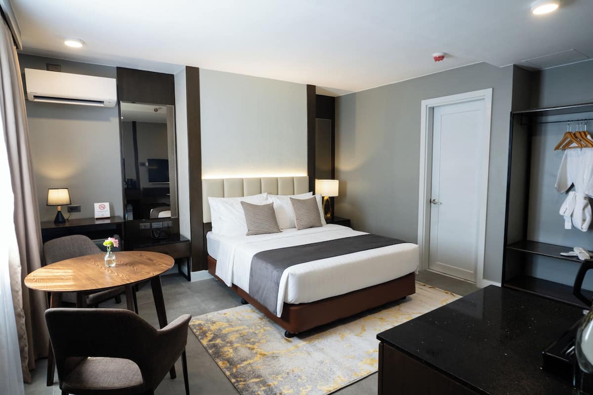 A hotel room with a bed, bedside table, lamp, chair, and a small round table with a vase.