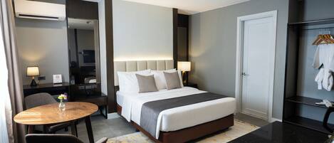 A hotel room with a bed, bedside table, lamp, chair, and a small round table with a vase.