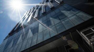 Un bâtiment moderne doté d’une façade en verre, et où le soleil brille intensément à travers les fenêtres.