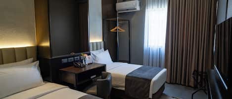 Quarto de hotel com duas camas, uma mesa, uma cadeira, uma televisão e um espelho grande.