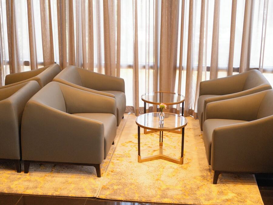 A modern lounge area with leather armchairs, a glass coffee table, and a view through sheer curtains.