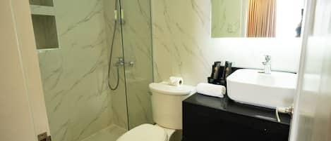 Un baño con inodoro, ducha con cerramiento de vidrio, lavamanos y espejo.