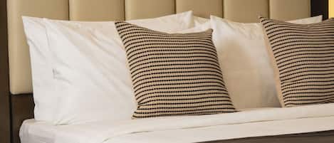 Una cama bien hecha con cabecera, ropa de cama blanca y dos almohadas estampadas.