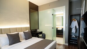 Et moderne hotelværelse med en stor seng, et sengebord og et walk-in closet med spejl og ophængte badekåber.