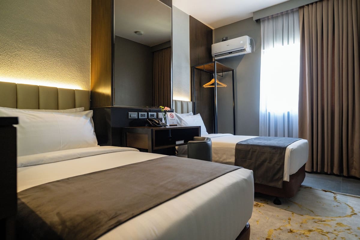 A hotel room with two beds, a desk with a phone and a coffee maker, an air conditioning unit, and a large mirror.
