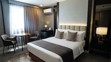 Een hotelkamer met een bed, bureau, stoel, lamp en een raam met gordijnen.