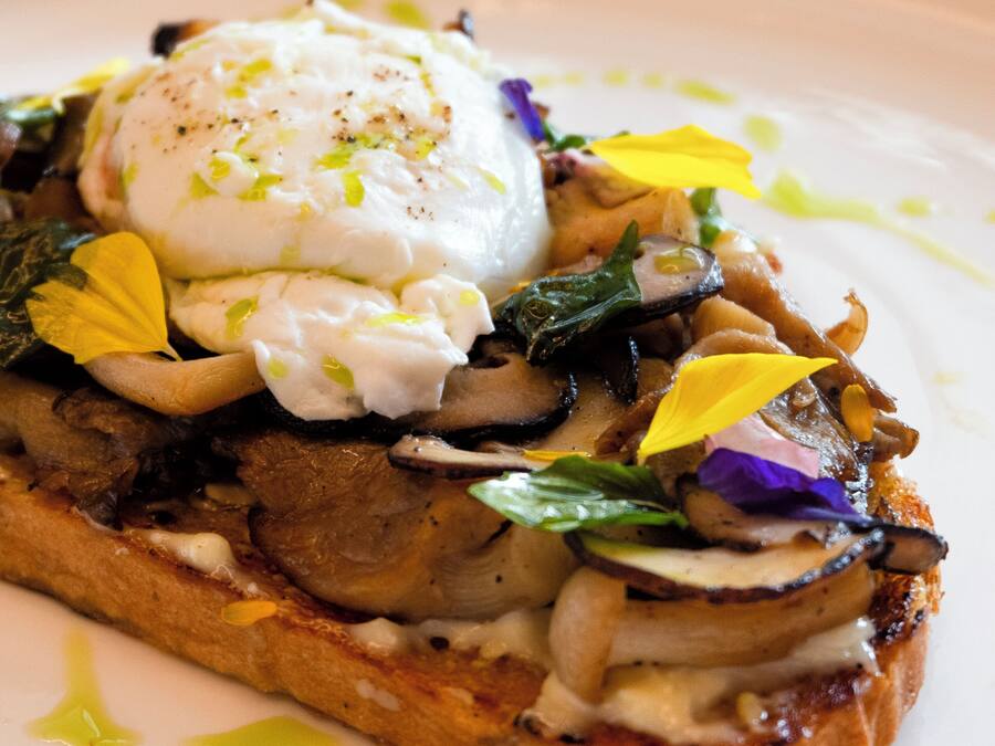 A dish with poached eggs, mushrooms, and greens on toast, served on a white plate.