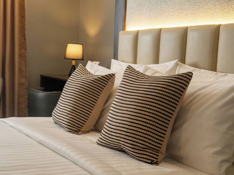 Ein Hotelzimmer mit einem Bett, zwei gestreifte Kissen, einem Nachttisch mit Lampe und einem Sessel.