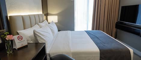 A hotel room with a bed, a desk, a chair, a TV, and a 'No Smoking' sign.