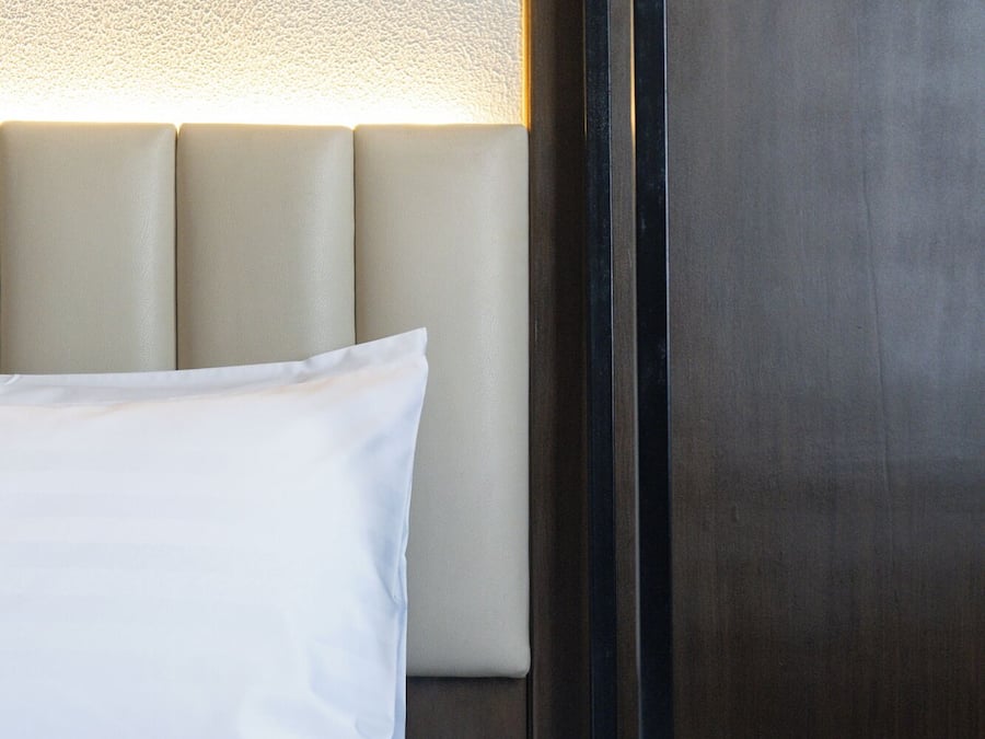 A neatly made bed with white linens and a headboard with a light-colored padded backrest.