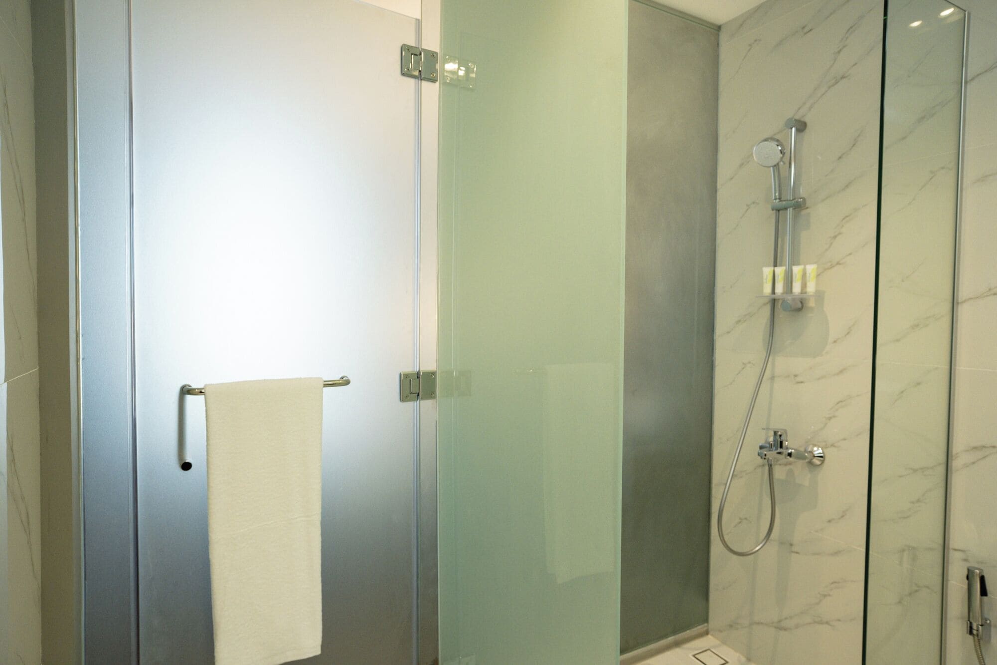 A modern bathroom with a glass shower enclosure, a towel rack, and marble walls.