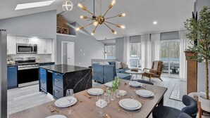 A modern kitchen with a central island, a dining area with a table set for six, and a living area with a sofa and a chair. - Pocono Blue | Paddleboards, Spa, Indoor Jacuzzi, GameRoom, Lake, EV (Clifton Township)