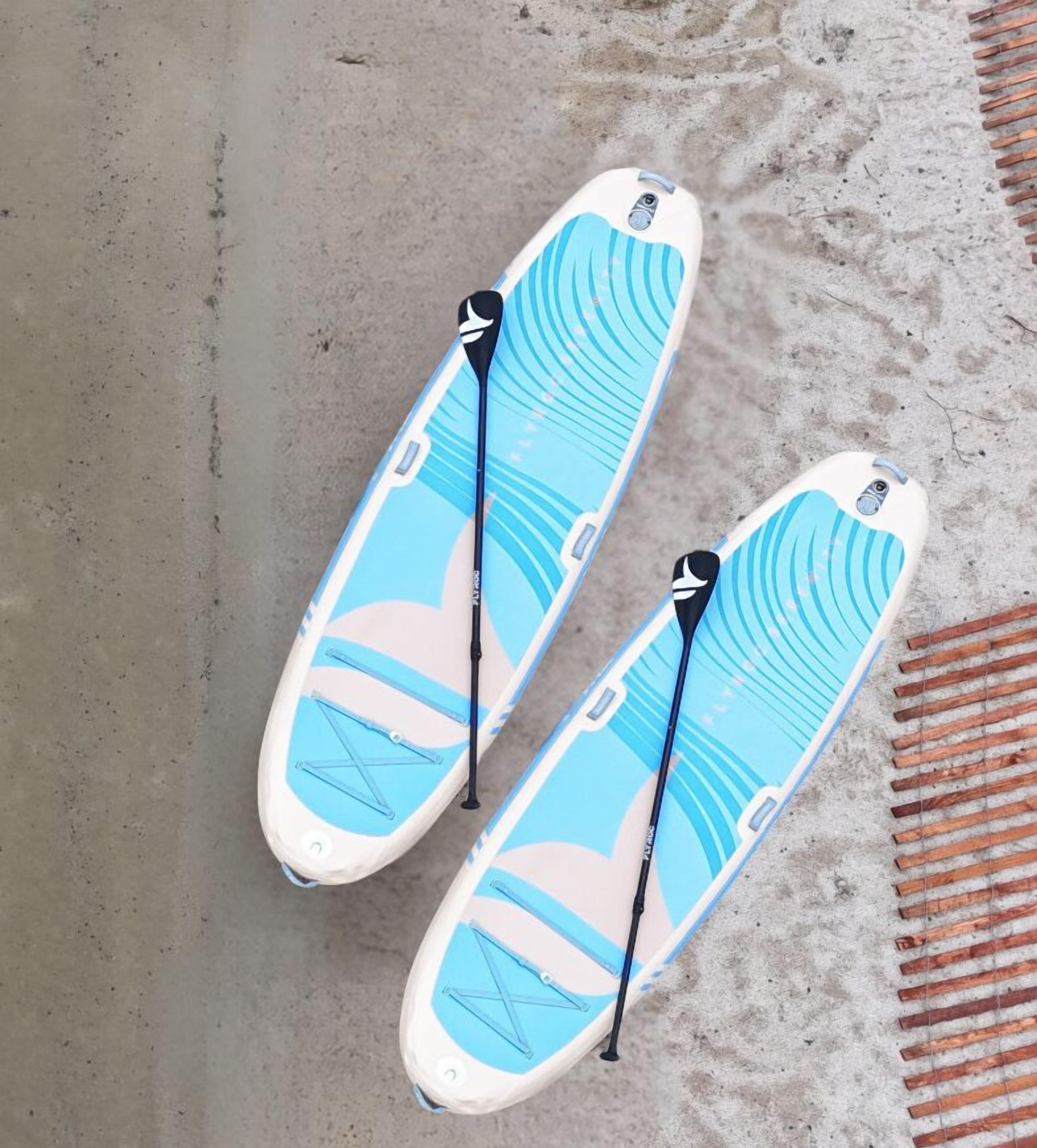 Dos tablas de paddleboard con diseños azules y blancos sobre una superficie de concreto.