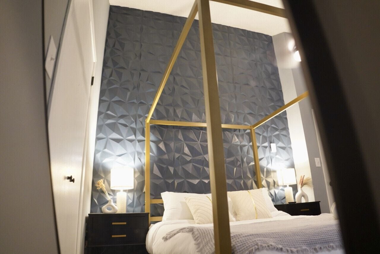 Une chambre à coucher avec un mur orné d’un motif géométrique, un lit à baldaquin et des tables de chevet avec des lampes.