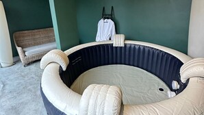 Un jacuzzi rond, avec un intérieur foncé et des coussins extérieurs de couleur claire, installé devant un mur vert et agrémenté d’un plafond en bois.
