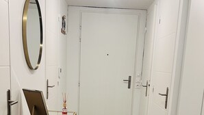 Een hal met witte deuren, een glazen tafel met een schilderstatief, en een spiegel aan de muur.