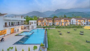 A resort with a swimming pool, outdoor seating, and a view of mountains. - Evara Spa & Resort (Ramnagar)