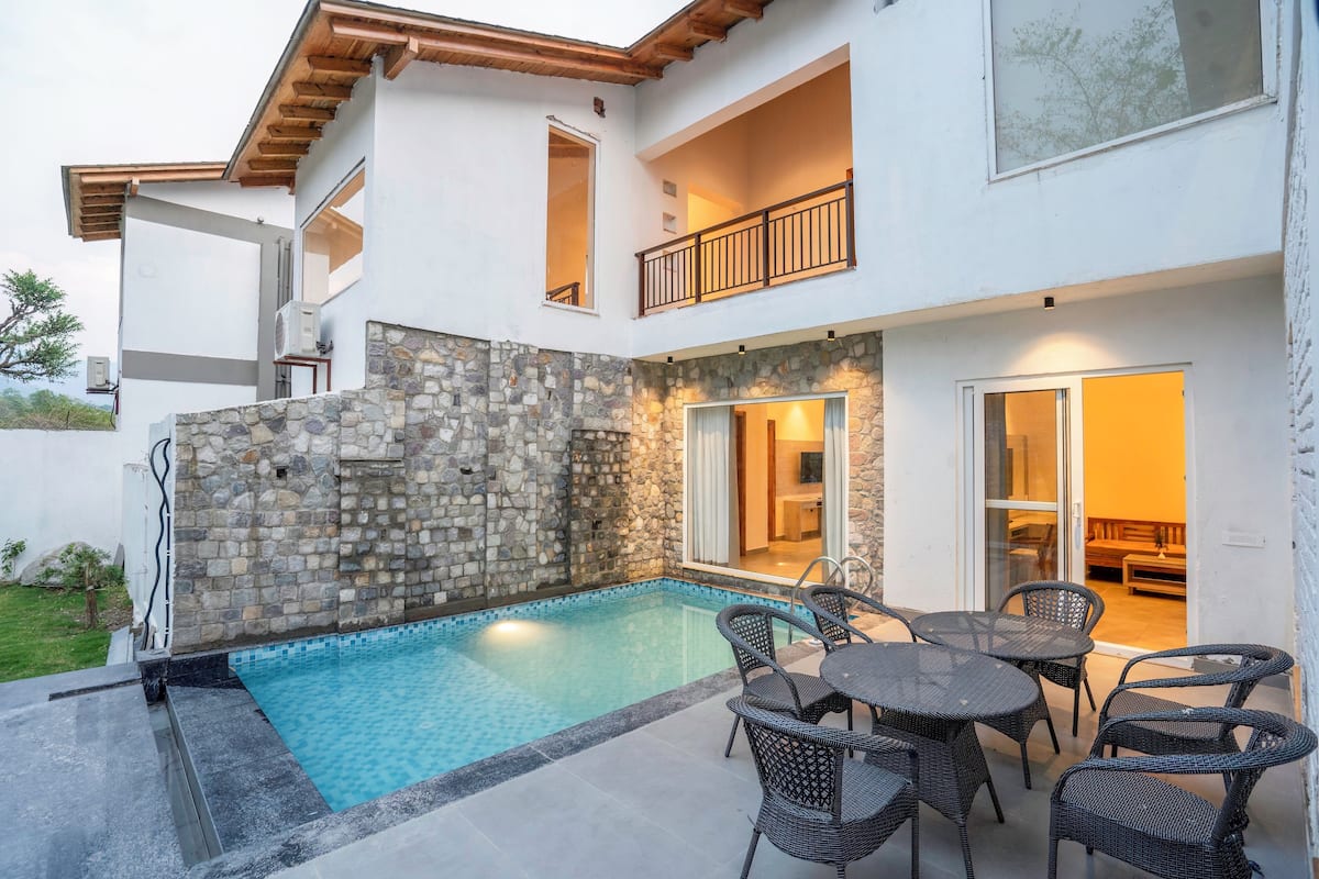 A modern house with a stone exterior, a swimming pool, and outdoor furniture.