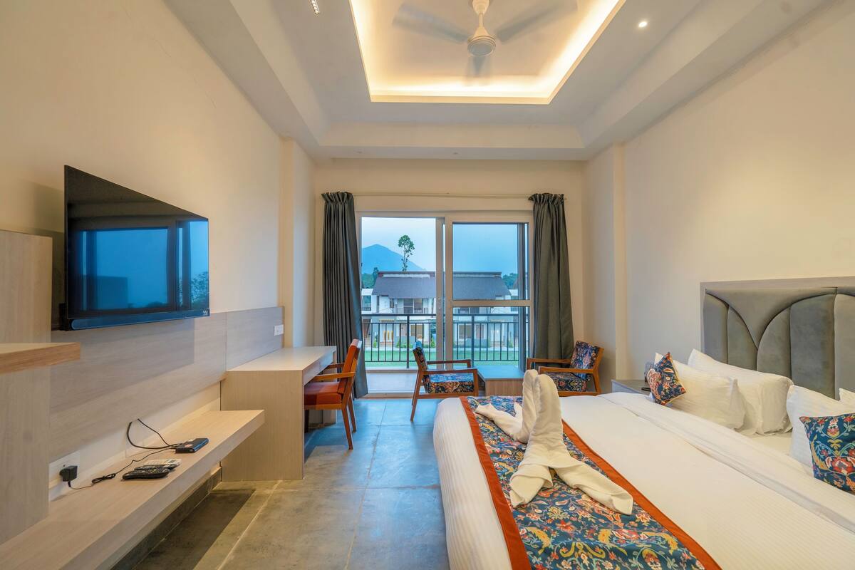 A hotel room with a bed, a desk, a TV, and a balcony with a view of a mountain.