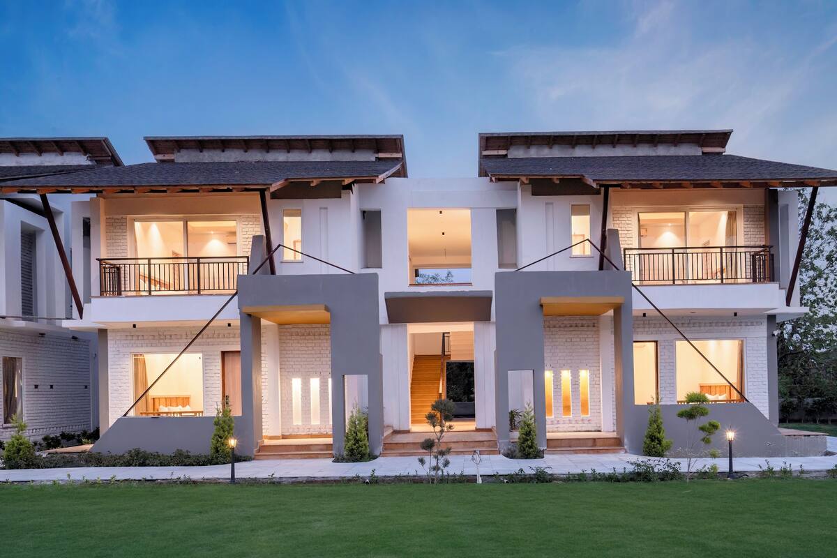 A modern two-story house with a central entrance, balconies, and a well-lit front yard.