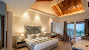 A modern hotel room with a large bed, a desk, and a balcony with a view. - Evara Spa & Resort (Ramnagar)