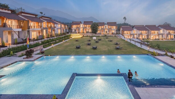 A hotel with multiple guest rooms, a swimming pool, and a well-maintained lawn area. - Evara Spa & Resort (Ramnagar)
