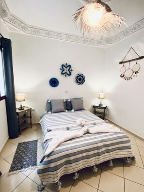 Ein Schlafzimmer mit einem Bett, zwei Nachttischen, einem gemusterten Teppich und Wanddekorationen.