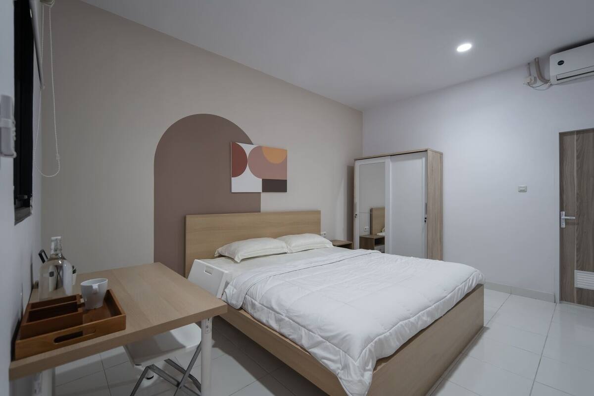 Un dormitorio con cama, escritorio, silla, armario y una obra de arte colgada en la pared.