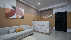 Un área de recepción con un mostrador de mármol, un sofá gris con un cojín de color mostaza y arte abstracto en la pared.
