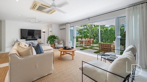 Un salon moderne doté d’un grand téléviseur à écran plat, d’un canapé, d’une table basse et offrant une vue sur un patio aménagé avec du mobilier d’extérieur.