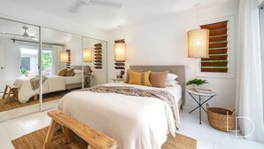 Une chambre moderne avec un grand lit, un miroir, un ventilateur de plafond et une table de chevet avec une lampe.