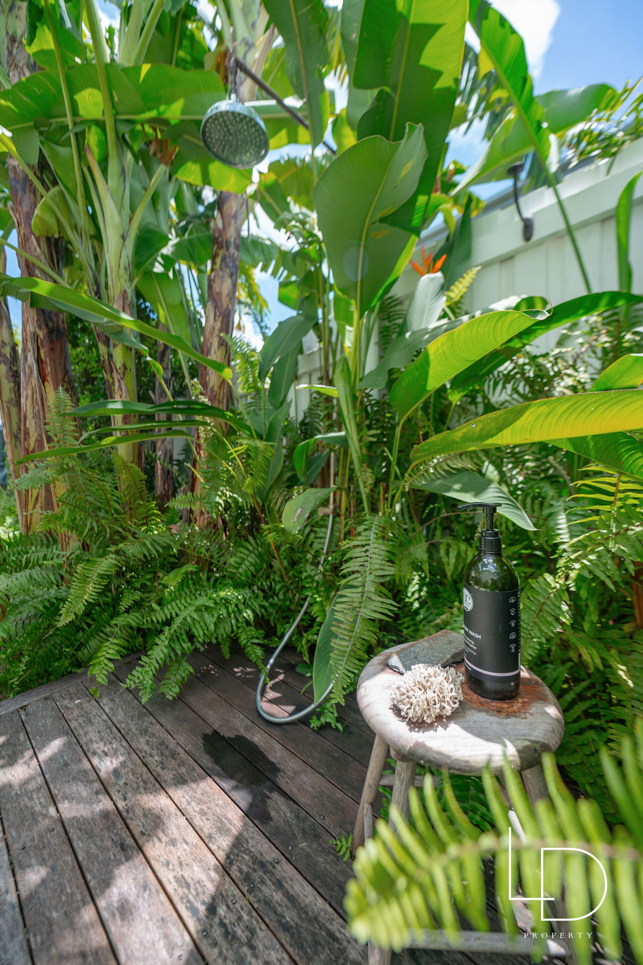 Una terraza de madera rodeada de exuberante vegetación tropical, con una mesa pequeña, una botella y un objeto decorativo.