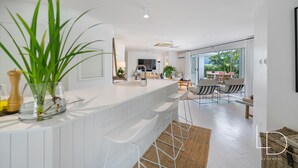 Une cuisine moderne avec un plan de travail blanc, des tabourets de bar et une grande plante verte.