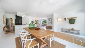 Une cuisine moderne avec des meubles blancs, une table à manger en bois et un grand vase vert.
