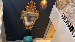 Un escalier avec un mur sombre, un grand miroir doré et deux luminaires suspendus.