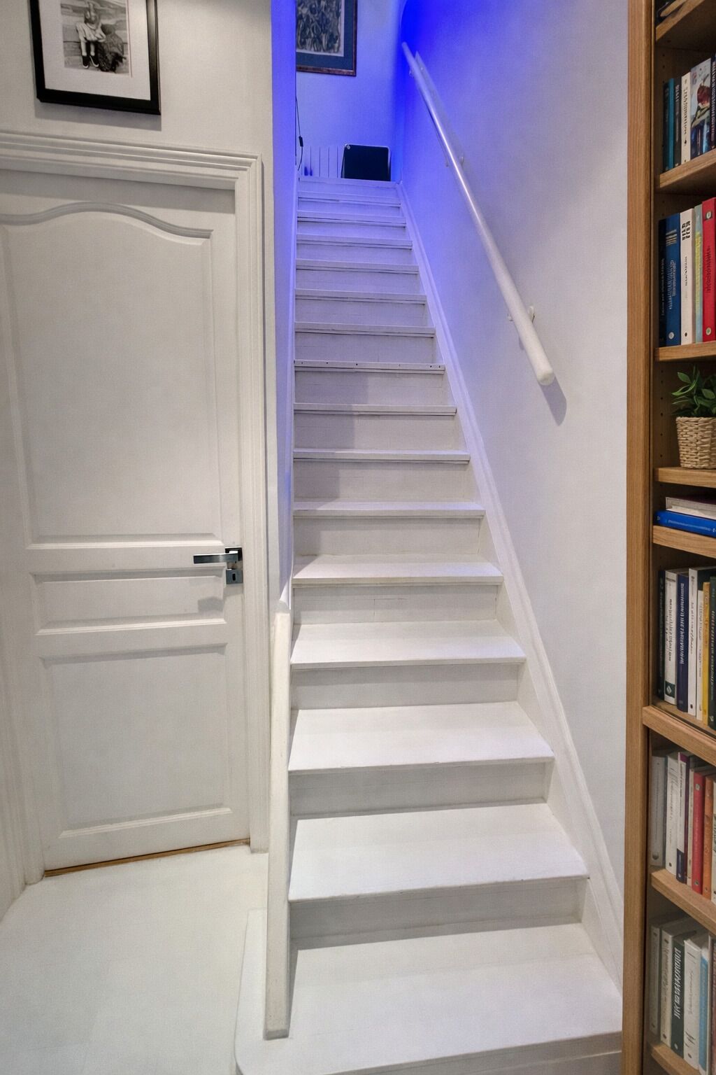 A white staircase with a handrail, leading to a landing. A bookshelf with books is visible to the right.
