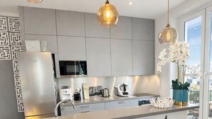 Et moderne køkken med central ø, rustfrie stål hvidevarer og hængende lamper.