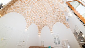 A spacious room with a high arched ceiling, white walls, and a kitchen area with a refrigerator and cabinets. - Elegance Staffa Rooms (Carovigno)