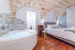 Un dormitorio con techo de piedra, una bañera grande, un armario de madera y una cama con ropa de cama blanca.