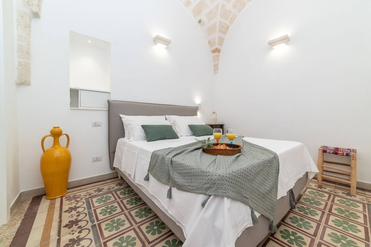 Een slaapkamer met een bed, nachtkastje en een klein krukje.