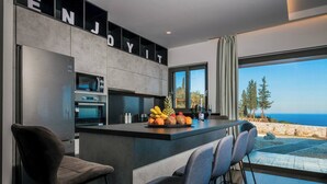 A modern kitchen with a central island, bar stools, and a view of the sea. - Nikolakos Villa - Pirvate Pool (Zakynthos)