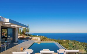 En modern villa med pool, utomhusmöbler och utsikt över havet.
