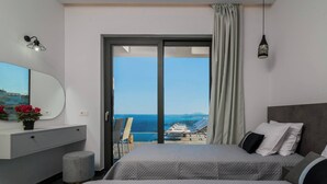 A hotel room with a bed, a desk, a chair, a small stool, and a view of the sea. - Nikolakos Villa - Pirvate Pool (Zakynthos)