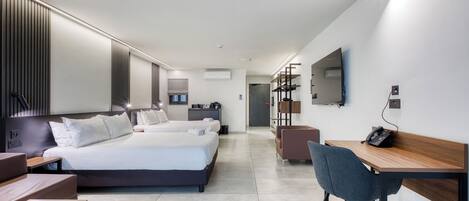 A modern hotel room with two beds, a desk, a chair, and a flat-screen TV.