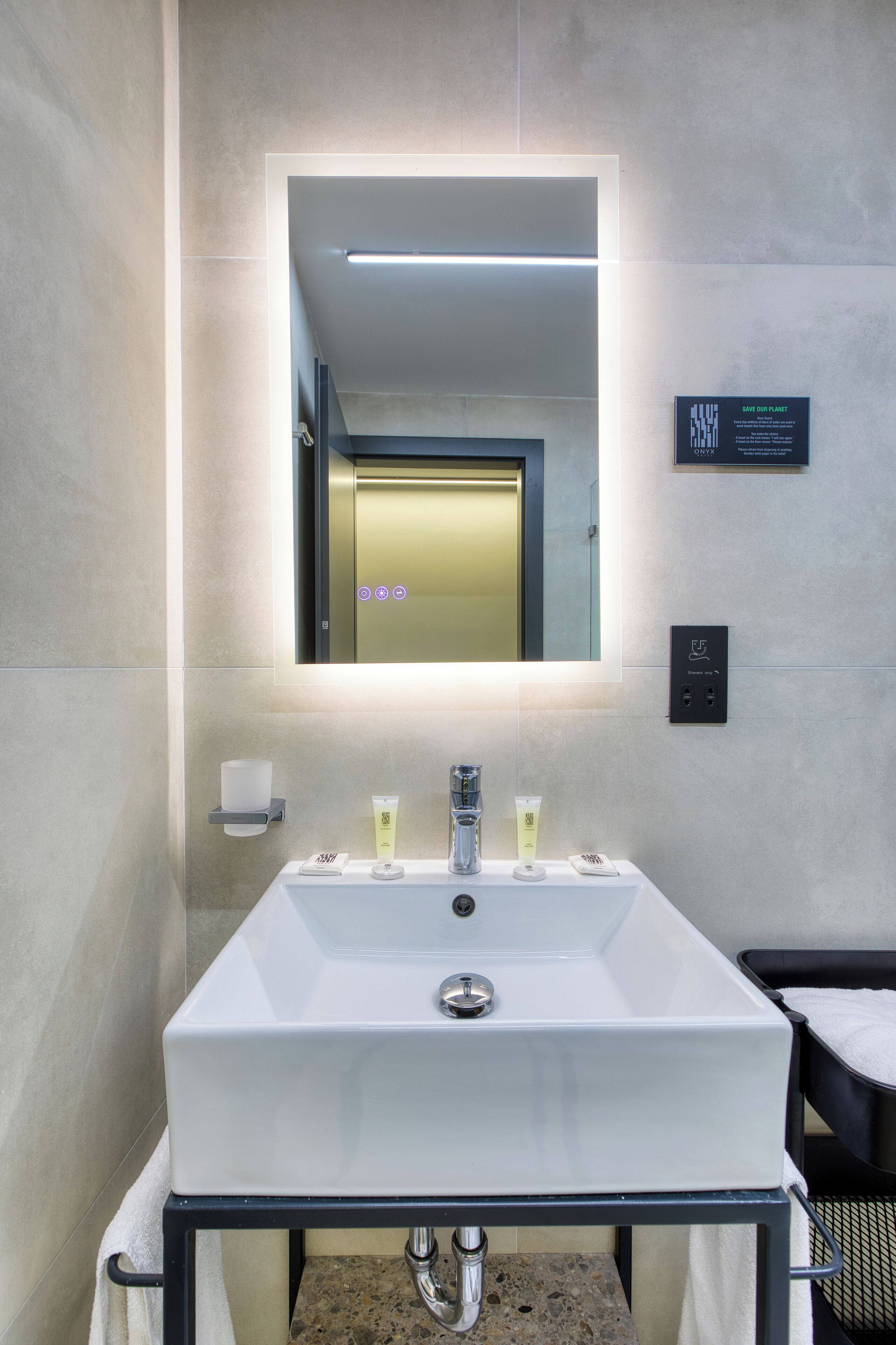 A modern bathroom with a large mirror, a white sink, and a towel rack.