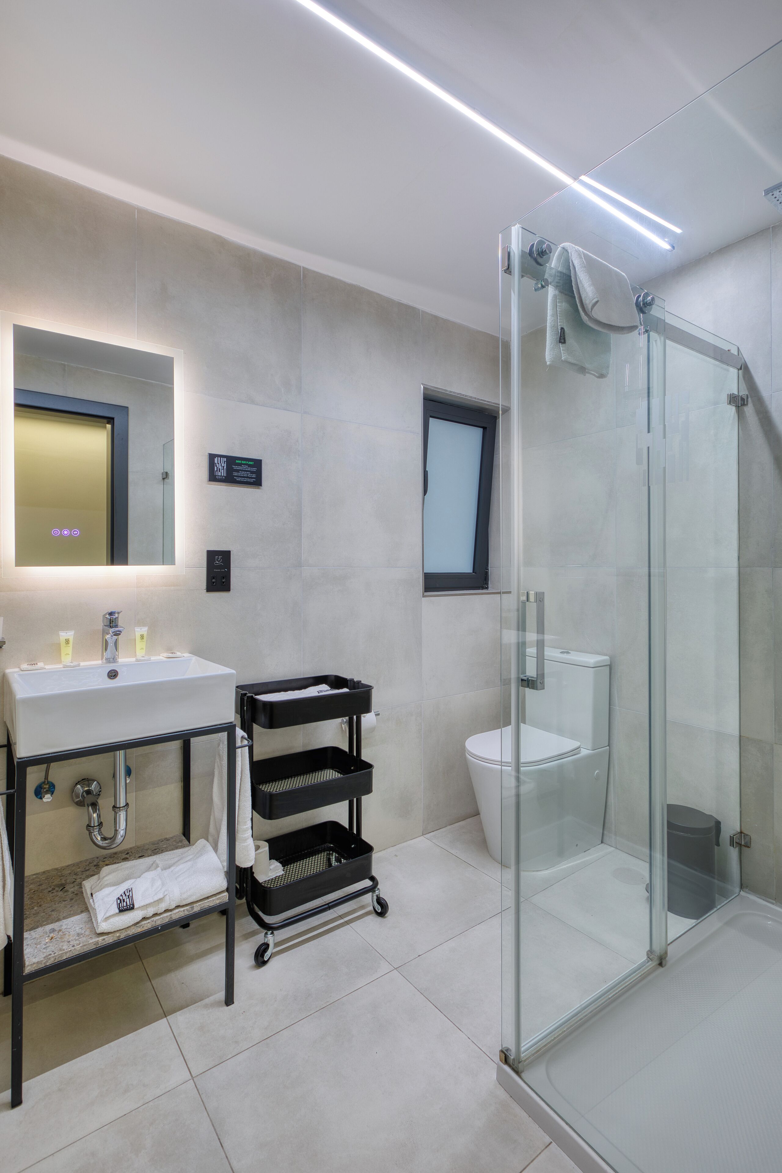 A modern bathroom with a glass-enclosed shower, a sink with a mirror, and a black cart with towels.