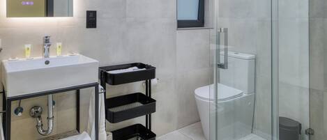 A modern bathroom with a glass-enclosed shower, a sink with a mirror, and a black cart with towels.