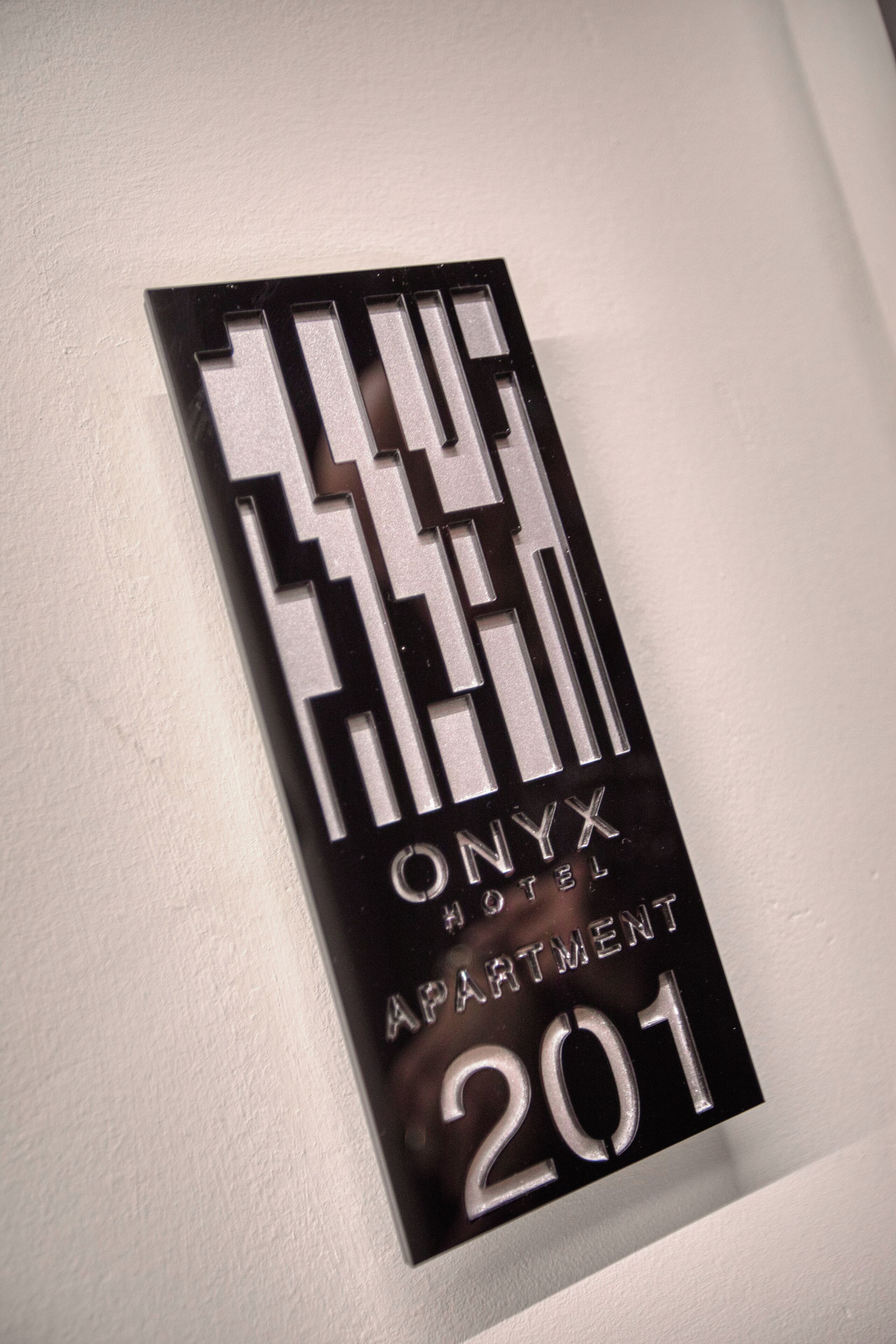 Ein schwarzes Schild mit weißer Schrift, das „ONYX HOTEL APARTMENT 201“ angibt.