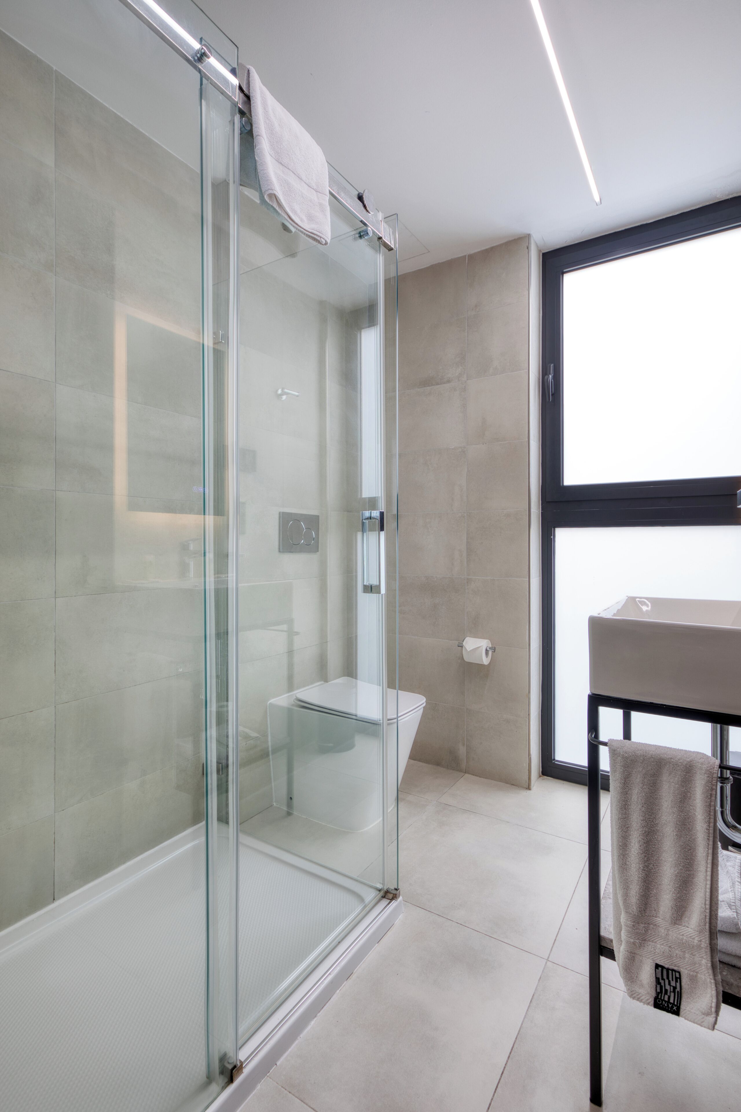 A modern bathroom with a glass shower enclosure, a toilet, and a sink with a towel on the counter.