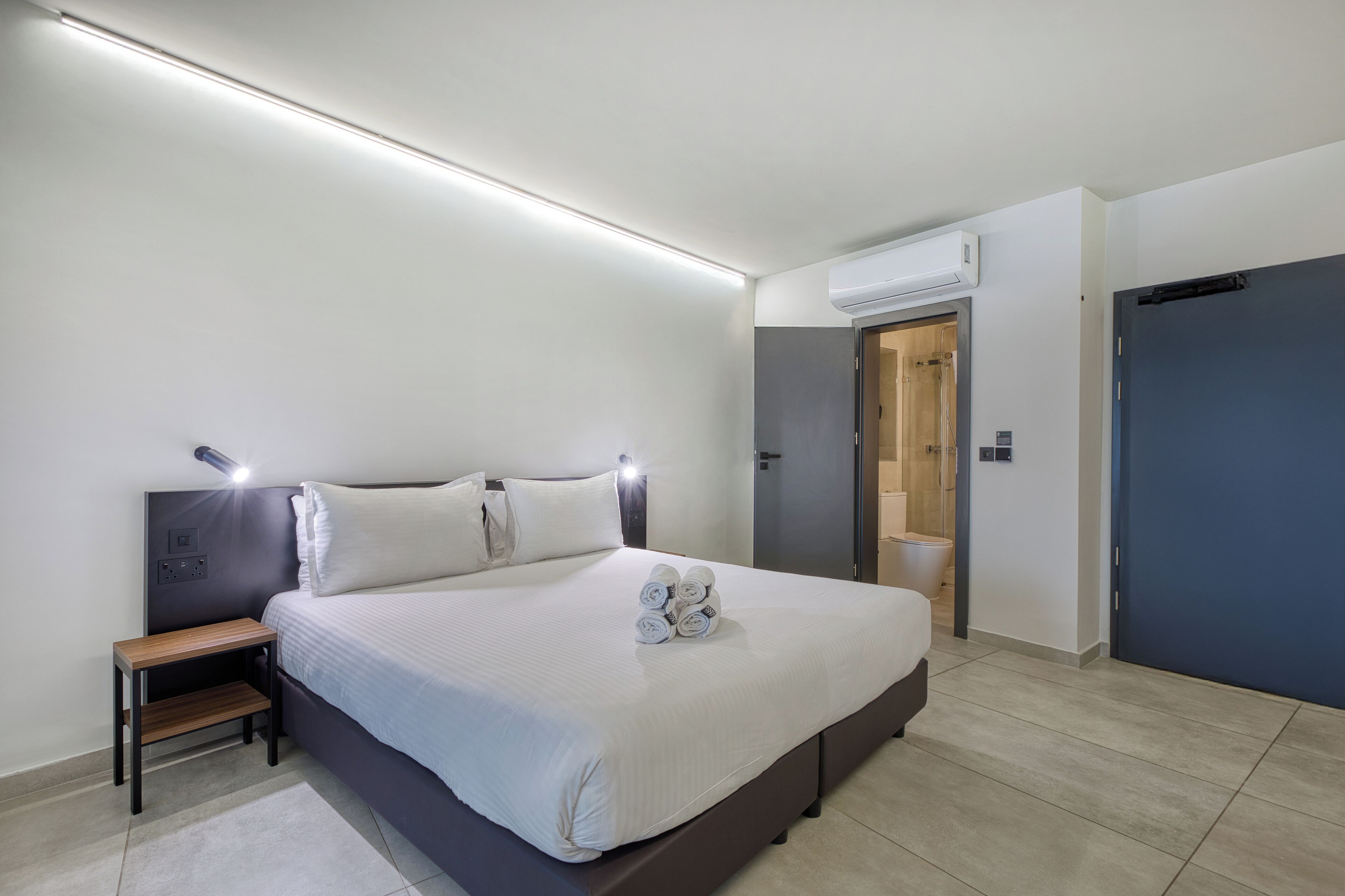 Ein modernes Hotelzimmer mit einem großen Bett, Nachttischen, einem Kleiderschrank und einer Klimaanlage.